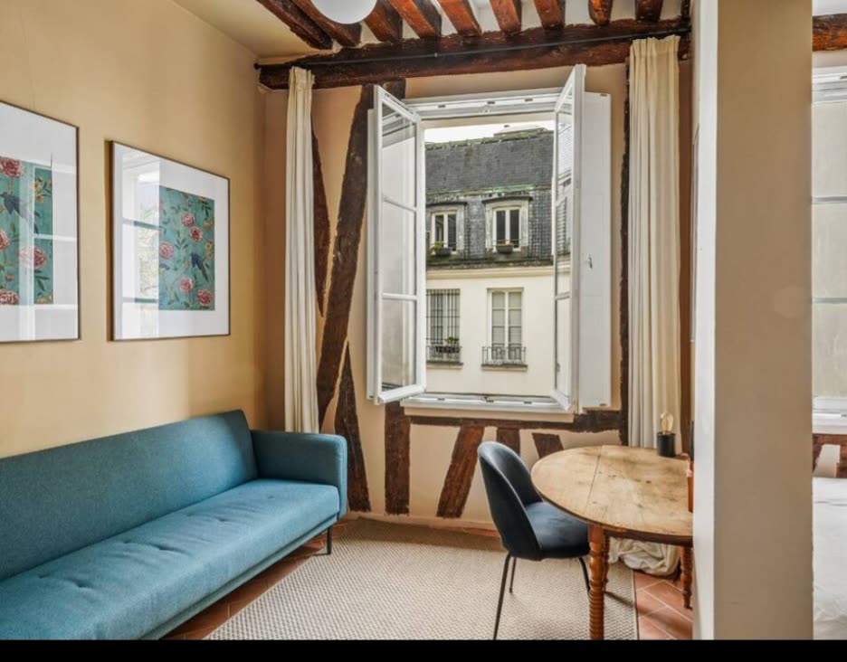 Living area with original exposed beams and open windows over a Parisian courtyard