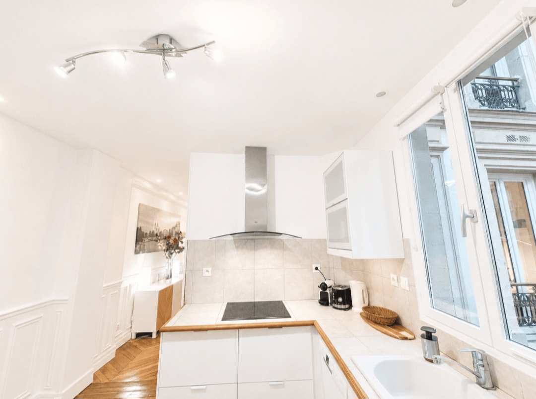 Kitchen with ceramic hob, extractor hood and window onto a Haussmann façade — Le Marais · Paris 4e