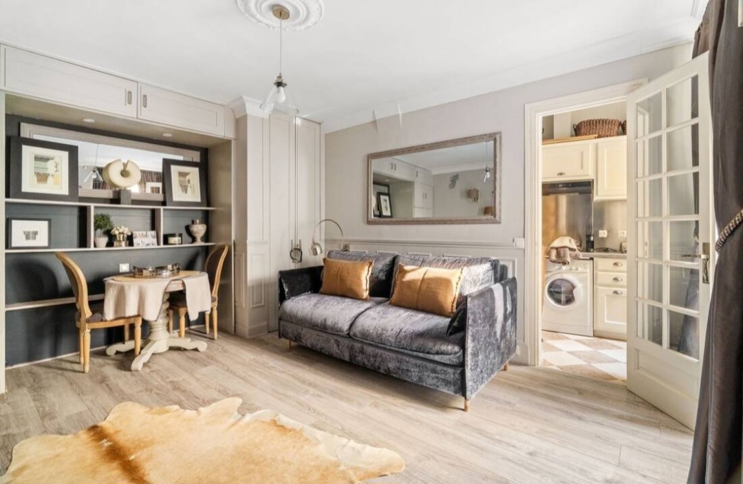 Living and dining area with bistro table, built-in joinery and glazed door to the kitchen — Rue du Bac · Paris 7e