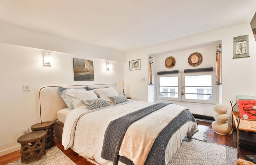 Bedroom with double bed, soft headboard and window onto a quiet Paris 1st street