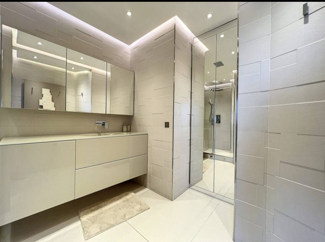 Stone bathroom with walk-in shower and backlit mirrors